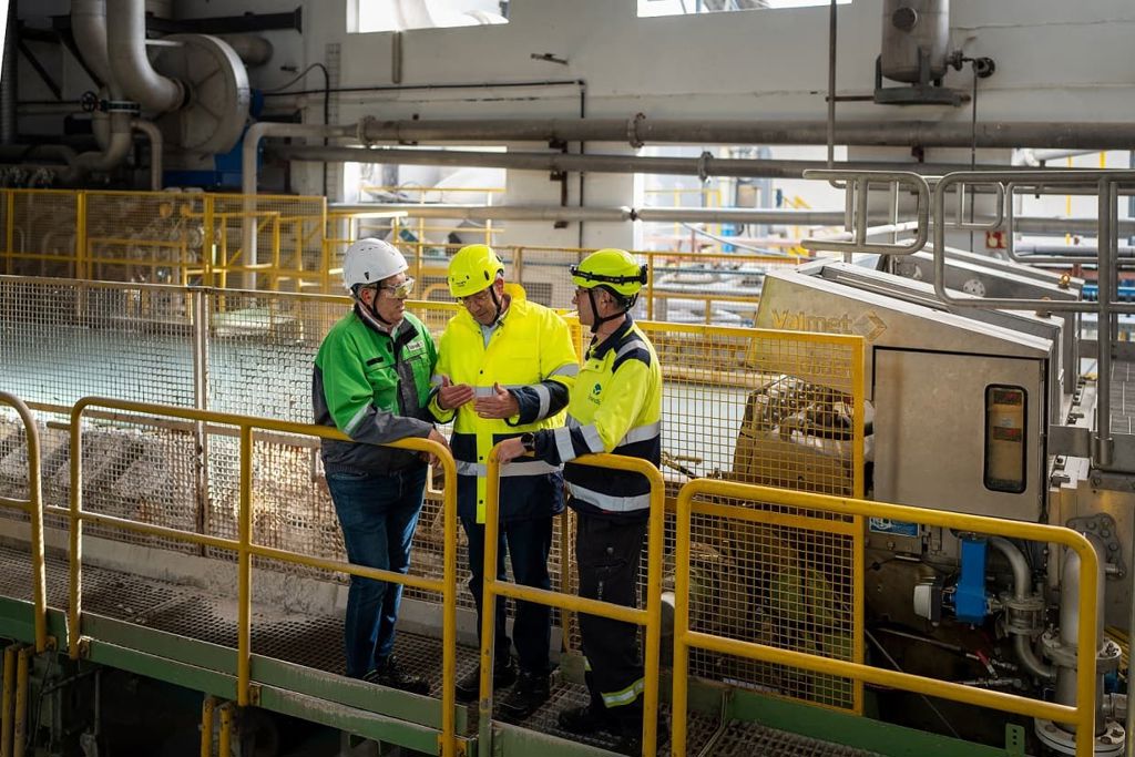 Three men standing in front of a specialty paper machined wet end