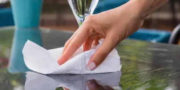 A hand using a tissue to wipe up water from a smooth surface.
