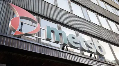 The exterior of a modern building featuring large windows and a metallic facade displays a prominent sign with the Metso logo. The logo consists of a stylized red and white graphic element next to the word "metso" in bold gray letters, identifying the company's branding on the building, located at Fabiankatu.