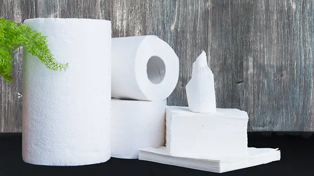 A selection of tissue products, including toilet paper rolls and folded paper towels, arranged on a black surface.
