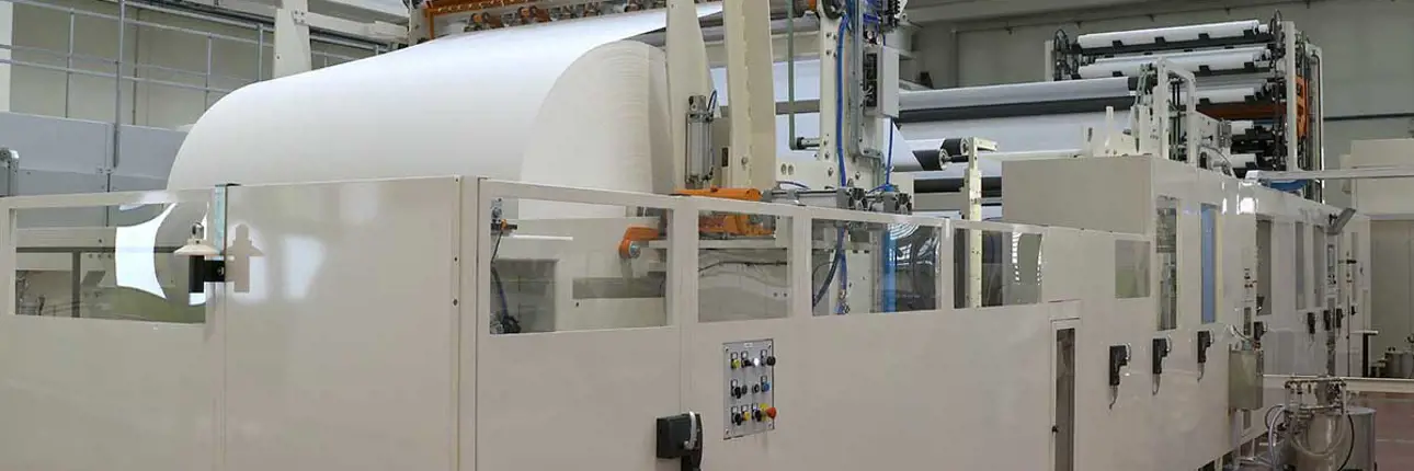 An industrial paper converting machine processing a large tissue paper roll inside a production facility.