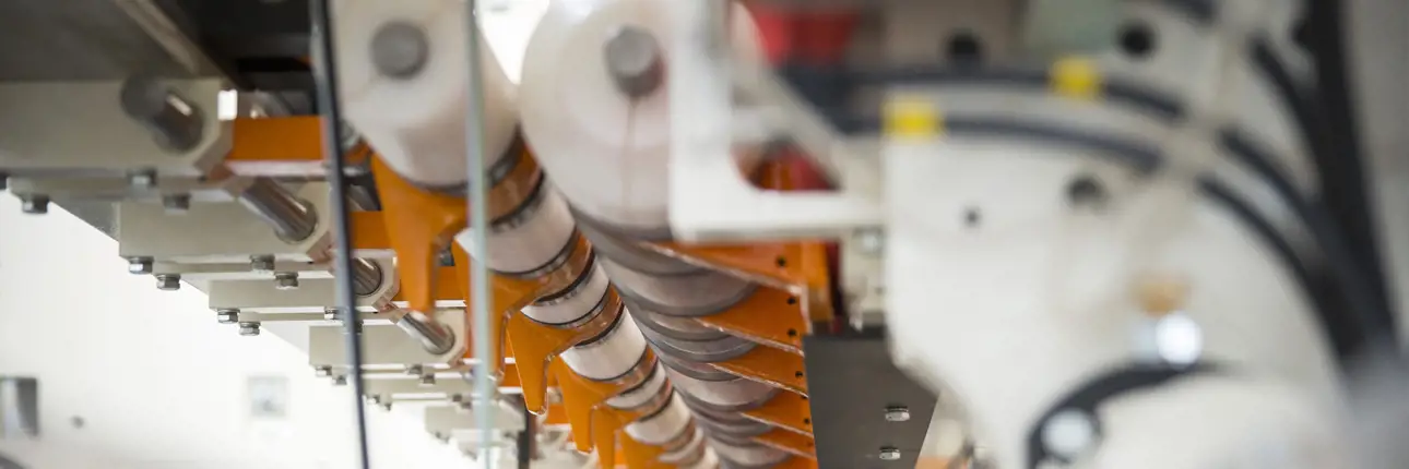 Close-up of a row of synchronized rotary blades or rollers in a tissue converting machine, guiding and processing paper rolls.